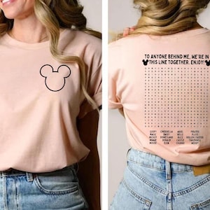 Pode incluir: Camiseta rosa claro com um contorno preto do Mickey Mouse na frente. A parte de tr&aacute;s da camisa tem um jogo de palavras com palavras tem&aacute;ticas da Disney e o texto "TO ANYONE BEHIND ME, WE'RE IN THIS LINE TOGETHER. ENJOY!"