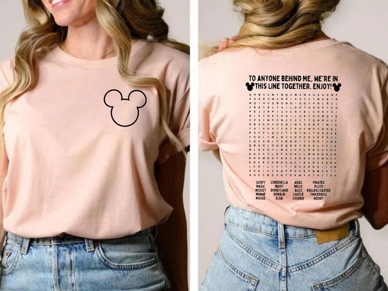 Pode incluir: Camiseta rosa claro com um contorno preto do Mickey Mouse na frente. A parte de tr&aacute;s da camisa tem um jogo de palavras com palavras tem&aacute;ticas da Disney e o texto "TO ANYONE BEHIND ME, WE'RE IN THIS LINE TOGETHER. ENJOY!"