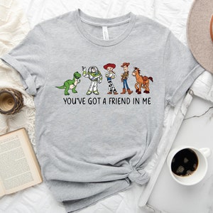 May include: Gray t-shirt with a print of characters from the Toy Story movie. The characters are lined up from left to right: Rex, Buzz Lightyear, Woody, and Bullseye. The text "You've got a friend in me" is printed below the characters.