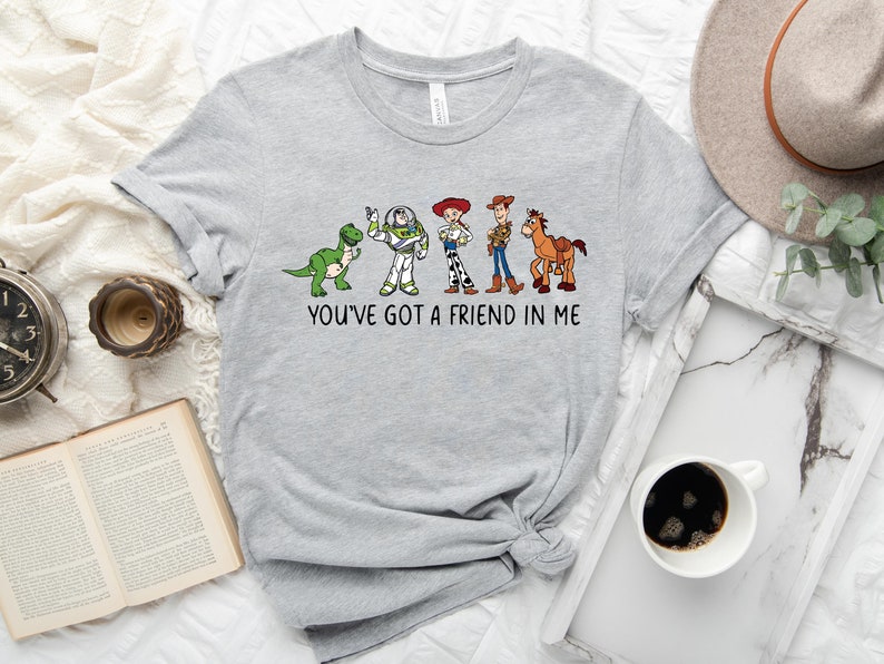 May include: Gray t-shirt with a print of characters from the Toy Story movie. The characters are lined up from left to right: Rex, Buzz Lightyear, Woody, and Bullseye. The text "You've got a friend in me" is printed below the characters.