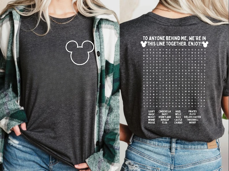 Pode incluir: Camiseta cinza escuro com um contorno branco do Mickey Mouse na frente. A parte de tr&aacute;s da camisa apresenta um quebra-cabe&ccedil;a de palavras com palavras tem&aacute;ticas da Disney e o texto "TO ANYONE BEHIND ME, WE'RE IN THIS LINE TOGETHER. ENJOY!"