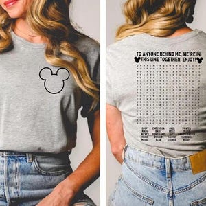 Pode incluir: Uma camiseta cinza com um contorno preto do Mickey Mouse na frente e uma busca de palavras nas costas. A parte de tr&aacute;s da camisa tem o texto "TO ANYONE BEHIND ME, WE'RE IN THIS LINE TOGETHER. ENJOY!"