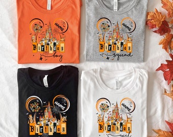 May include: Four t-shirts with a Halloween-themed design featuring a Mickey Mouse ear silhouette with a castle inside. The shirts are in orange, grey, black, and white. The text on the shirts reads "Birthday boy", "Birthday squad", "Birthday crew", and "Birthday girl".