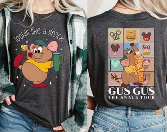 Puede incluir: Camiseta gris oscuro con un ratón de dibujos animados sosteniendo queso y una taza verde, con el texto "lookin' like a snack". La parte posterior de la camiseta tiene una cuadrícula de bocadillos y el texto "Gus Gus The Snack Tour".