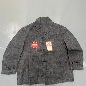 May include: A grey work jacket with a button-up front, lapel collar, and long sleeves. The jacket has two pockets and a small tag on the chest. A red and white "HANFOR" patch is visible on the left chest.