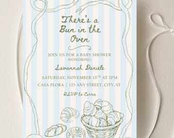 Puede incluir: Invitación para baby shower con fondo a rayas azules y blancas. La invitación presenta el texto "There's a Bun in the Oven" e incluye detalles del evento: nombre de la homenajeada, fecha, hora y lugar. Se ilustra una cesta de productos horneados.