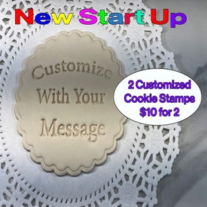 May include: A white, round cookie stamp with the text "Customize With Your Message" in a circular design. The text "2 Customized Cookie Stamps $10 for 2" is in a purple box in the upper right corner of the image.