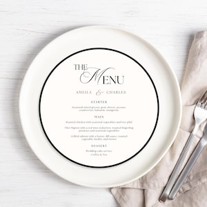 Può includere: Un piatto bianco con un bordo circolare nero mostra un menu per "Amelia & Charles". Il menu elenca le opzioni di antipasti, piatti principali e dessert. Una forchetta e un coltello poggiano su un tovagliolo di lino beige a destra.