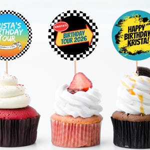 May include: Three cupcakes with decorative toppers. The toppers have text that reads "Krista's Birthday Tour" and "Happy Birthday Krista!" The cupcakes have white frosting and are decorated with a strawberry, an Oreo cookie, and red sprinkles.