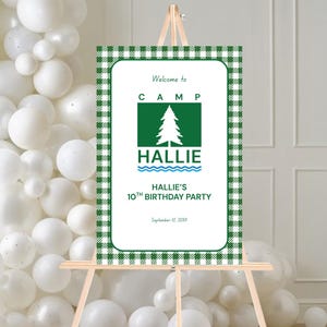 Pode incluir: Uma placa de boas-vindas para uma festa de aniversário. A placa tem uma borda xadrez verde e branca e apresenta o texto "Welcome to CAMP HALLIE" com um gráfico de árvore. Também diz "HALLIE'S 10TH BIRTHDAY PARTY". A placa está em um cavalete de madeira.