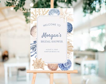 May include: A bridal shower welcome sign on an easel. The sign features a watercolor design of seashells and coral in shades of blue, beige, and brown. The text reads "Welcome to Morgan's Bridal Shower".