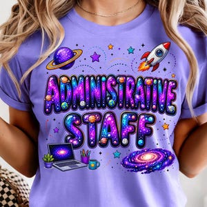 May include: A light purple t-shirt featuring the text "ADMINISTRATIVE STAFF" in a galaxy-themed font. The graphic includes a rocket ship, a planet with rings, a spiral galaxy, a laptop, a small potted plant, a pencil holder, and a coffee mug.