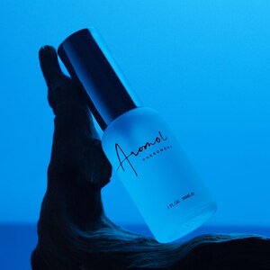 Puede incluir: Una botella de vidrio esmerilado azul claro con tapa negra, etiquetada "Aromol Pheromone" en escritura cursiva. La botella es de 30 ml y est&aacute; colocada sobre un fondo azul y un elemento de madera oscura texturizada.