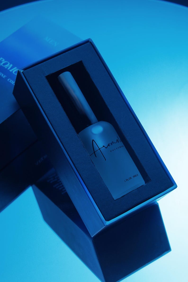 Puede incluir: Imagen azulada de un frasco de perfume en una caja azul oscuro. El frasco esmerilado tiene la palabra "Aroma" en cursiva. La caja est&aacute; en &aacute;ngulo, mostrando el frasco y su sombra. El texto "1 FL OZ 30ml" es visible.