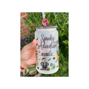 May include: Frosted glass tumbler with a black and white rhinestone-studded rim, featuring a Halloween-themed design. The tumbler has the words "Spooky Adventure awaits..." and includes cartoon characters and a bat charm on the straw.