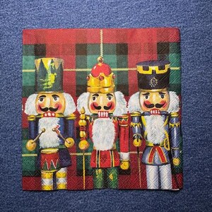 May include: Three nutcracker figurines with red, green, and blue accents stand against a red and green plaid background. The nutcrackers are wearing traditional costumes and holding musical instruments.