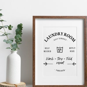 May include: A framed print with a laundry room sign that says "Laundry Room - Self Service - Help Needed - 5¢ - Apply Here - Wash - Dry - Fold - Repeat - Forever".