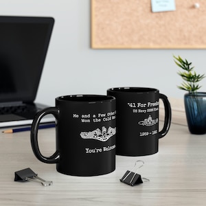 May include: Two black ceramic coffee mugs with white text and images. The mug on the left says "Me and a few others won the Cold War" and has a submarine insignia. The mug on the right says "41 For Freedom US Navy SSBN Fleet 1959-1991" and has a submarine image.