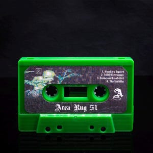 May include: Green cassette tape with a silver label that reads "Area Rug 51". The label also includes the song titles "Honkey Squirt", "1000 Elevators", "Tumcoat Enabilist", and "Flu Tortilla".