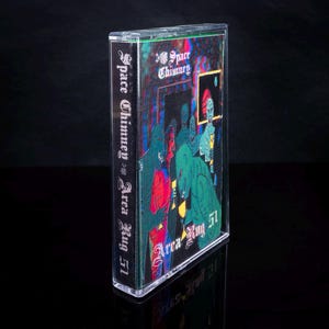 May include: A cassette tape with a black and green illustration of a group of people in front of a building with the text "Space Chimney vs Area Rug 51" on the side.