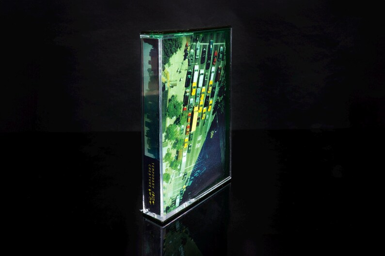 K&ouml;nnte beinhalten: Eine transparente Acrylbox mit einem gr&uuml;nen und gelben Bild einer Stadtstra&szlig;e. Das Bild zeigt eine Stra&szlig;e, die mit geparkten Autos und B&auml;umen ges&auml;umt ist.