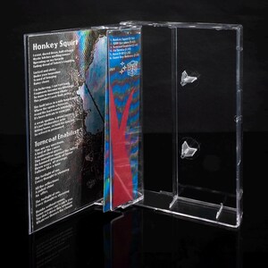 May include: A clear plastic cassette tape case with a colorful cassette tape inside. The cassette tape has the title "Honkey Squirt" and "Turncoat Enablist" printed on the front. The cassette tape has a blue, red, and black abstract design.