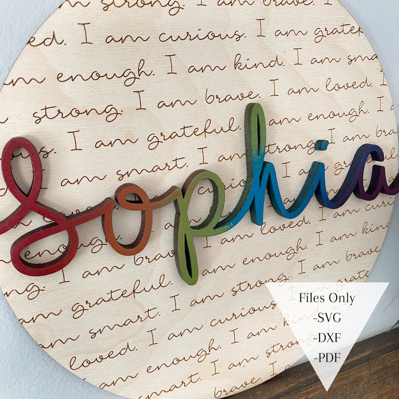 May include: A wooden circle with the name "Sophia" spelled out in rainbow colors. The background is covered in a repeating pattern of positive affirmations, such as "I am strong", "I am brave", "I am kind", and "I am loved".