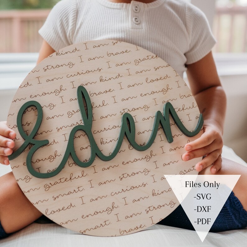 May include: A round wooden sign with the name "Eden" written in large green letters. The sign is covered in a repeating pattern of positive affirmations written in brown ink. The sign is being held by a child.