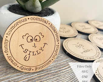 May include: A wooden coaster featuring a cartoon face and the word "Silly" written beneath. The coaster is encircled by text that reads "goofy, crazy, funny, humorous, amusing, playful, hilarious, comical".