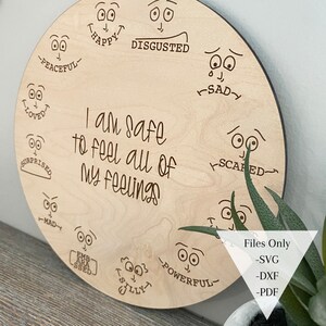 May include: A wooden circle with a variety of emotions drawn on it, including happy, sad, scared, surprised, mad, embarrassed, silly, powerful, disgusted, peaceful, and loved. The text "I am safe to feel all of my feelings" is written in the center of the circle.