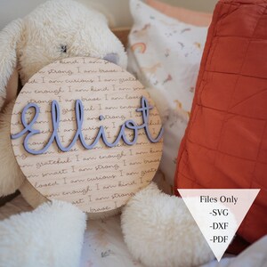 May include: A wooden round sign with the name "Elliot" written in purple script. The sign is surrounded by a circle of text that reads "I am kind, I am strong, I am brave, I am smart, I am curious, I am grateful, I am enough, I am loved."