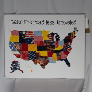 Könnte beinhalten: Ein weißer Leinwanddruck mit dem Text "take the road less traveled" über einem Patchwork-Design der Vereinigten Staaten.