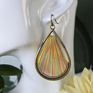 May include: A teardrop-shaped earring featuring an antique brass frame with a series of radiating, multicolored threads in shades of yellow, orange, green, and pink. The threads are anchored to the bottom of the frame through small, evenly spaced holes.