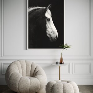 Puede incluir: Una fotograf&iacute;a en blanco y negro de la cabeza de un caballo de perfil, enmarcada y colgada en una pared blanca. El caballo est&aacute; mirando hacia la izquierda, con la cabeza ligeramente inclinada hacia abajo. El fondo es negro y la crin y la cola del caballo ondean con el viento.