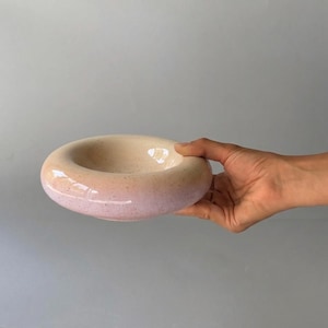 May include: A circular ceramic bowl with a smooth, rounded rim and a wide, shallow basin. The exterior features a gradient color transition from a soft cream tone at the top to a pale lavender hue at the base, accented by fine dark speckles.