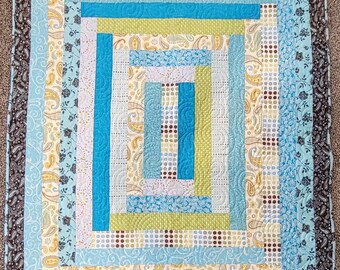 May include: A handmade quilt with a geometric design. The quilt features a central rectangular pattern in shades of blue, green, and white, surrounded by patterned borders. The border has a paisley design in shades of brown, blue, and yellow.