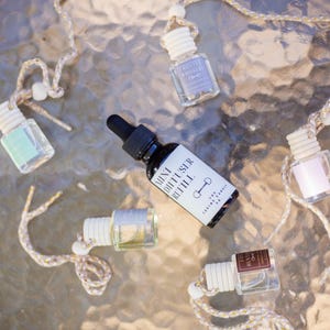 May include: An assortment of small glass diffuser bottles with white tops and attached cords. One bottle is black with a dropper and the text "Mini Diffuser Refill". Other bottles have labels with text like "Frosted Whiskers".