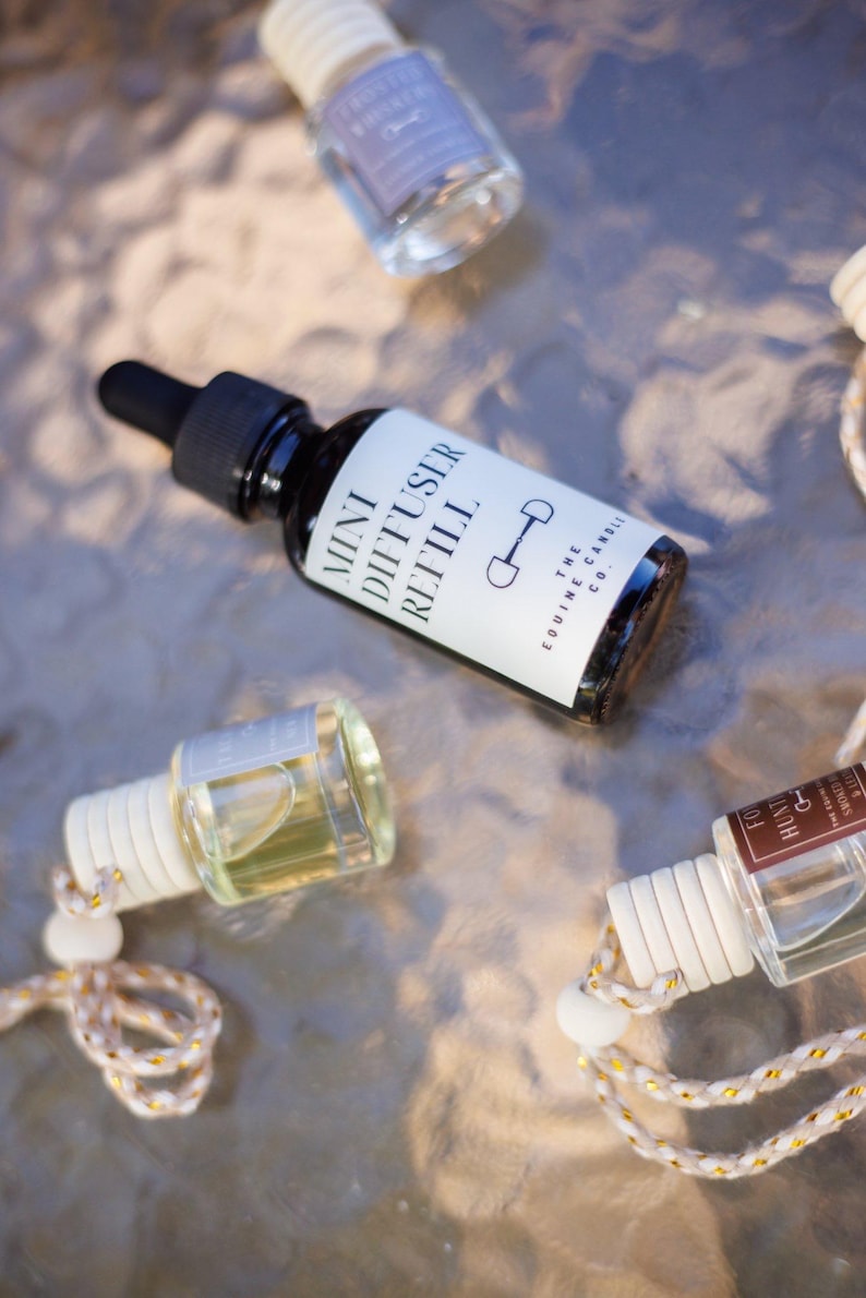 May include: A collection of mini diffuser refill bottles with black caps and white labels. One bottle is labeled "Mini Diffuser Refill" with a horse bit graphic. Other bottles have white tops and decorative cords.