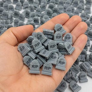 May include: A collection of small, gray, tombstone-shaped charms, each featuring the letters RIP embossed in black. These miniature grave markers are uniform in design, with a rounded top and a rectangular base, suitable for various decorative projects.