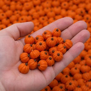 May include: A collection of small, bright orange miniature pumpkins with textured ridges and dark brown stems. Each pumpkin features a rounded shape and a distinct stem at the top, presented in a cluster of many identical pieces for decoration.