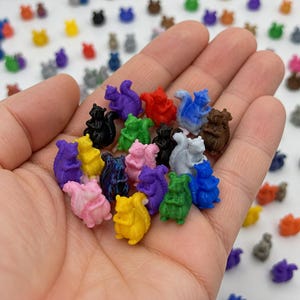 May include: A collection of small, miniature squirrel figurines in various solid colors including red, blue, green, yellow, purple, pink, black, and brown. Each tiny plastic squirrel is sculpted in a seated position with a bushy tail curved upward.