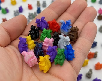 May include: A collection of small, miniature squirrel figurines in various solid colors including red, blue, green, yellow, purple, pink, black, and brown. Each tiny plastic squirrel is sculpted in a seated position with a bushy tail curved upward.