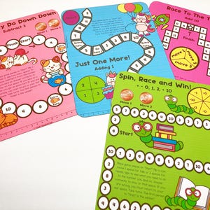 Puede incluir: Cuatro tableros de juego coloridos con diferentes temas: "Down Kitty Do Down Down", "Just One More!", "Race To The Top!" y "Spin, Race and Win!" Cada tablero presenta un dise&ntilde;o &uacute;nico con ilustraciones e instrucciones para jugar.