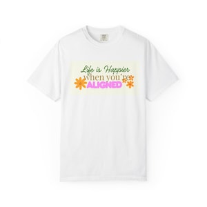 Può includere: T-shirt bianco con scollo tondo. La maglietta presenta la scritta "Life is Happier when you're ALIGNED" in verde e rosa, con fiori arancioni. Il disegno è su un rettangolo giallo chiaro.
