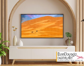 May include: A framed print featuring a desert landscape with two camels. The artwork, displayed on a white cabinet, showcases a vast expanse of orange sand dunes under a blue and pink sky. The print is labeled "BonVoyage DIGITALART."