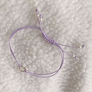 Puede incluir: Un brazalete de amistad morado con un dije de corazón plateado y cuentas plateadas.