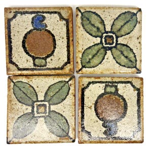 May include: Four square ceramic tiles with a speckled cream glaze. Two tiles feature a central brown circular motif with blue accents, while the other two display a four-petaled green leaf design outlined in dark brown.