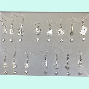May include: A collection of silver-toned musical instrument earrings, including guitars, a drum set, piano, treble clef, microphone, cassette tape, violin, trumpet, saxophone, and French horn. Each earring has a hook for easy wear.