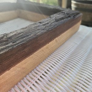 Könnte beinhalten: Ein rechteckiger Holzrahmen mit zweifarbigem Design. Der obere Teil besteht aus dunklem, verwittertem und strukturiertem Holz mit rauer Maserung, während der untere Teil aus glattem, hellem Naturholz mit einer sauberen Oberfläche gefertigt ist.