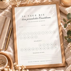 Può includere: Una stampa incorniciata che presenta una tabella per il conto alla rovescia di 30 giorni con testo in tedesco. Il design include cerchi numerati da 1 a 30, righe per un evento e una data, una sezione 'HALBZEIT' e la frase 'KLEINE SCHRITTE, GROSSE MOMENTE'.